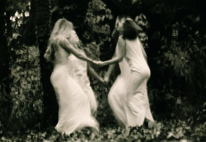 Vier junge Frauen tanzen im Wald und halten sich an den Händen (Schwarzweiß, verschwommene Bewegung)