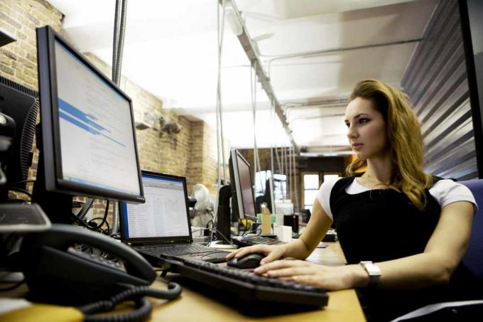 Eine Frau sitzt an einem Schreibtisch mit einem Laptop mit externer Tastatur und Monitor.