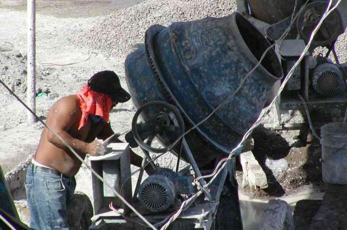 Mann in Jeans ohne Hemd, roter Schal unter Hut, arbeitet an einer kleinen, runden Maschine vom Typ Betonmischer