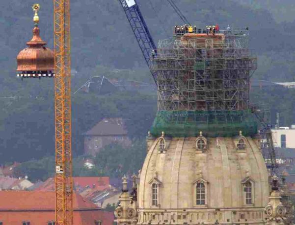 Ein Kran hebt die Kupferkuppel und das goldene Kreuz auf die rekonstruierte Frauenkirche in Dresden