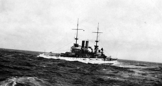 Schlachtschiff USS Wisconsin (BB-9), das in rauem Wasser mit Bogen durch eine große Welle dampft.