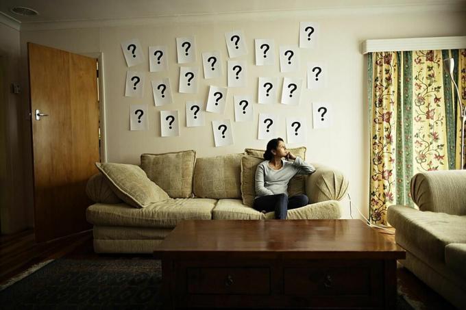 Mujer sentada en sofá con pared con símbolos de interrogación.