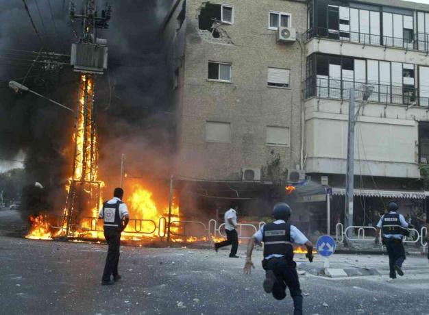 Israelische Polizisten eilen zum Schauplatz eines brennenden Strommasts und beschädigten Gebäude, kurz nachdem eine Salve von Hisbollah-Raketen am 13. Juli 2006 in der nördlichen Stadt Nahariya in Israel einschlug.