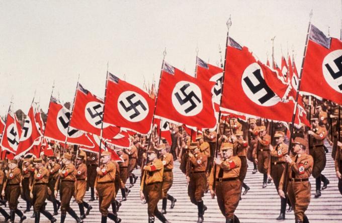 Nazis marschieren in Formation mit Flaggen bei einer Kundgebung.