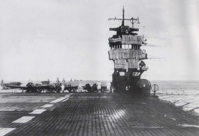 Flugdeck des Flugzeugträgers Akagi mit Insel rechts und an Deck geparktem Flugzeug.