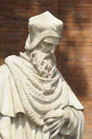 Eine weiße Statue eines älteren Nicholaus Copernicus, mit einer Mauer im Hintergrund.