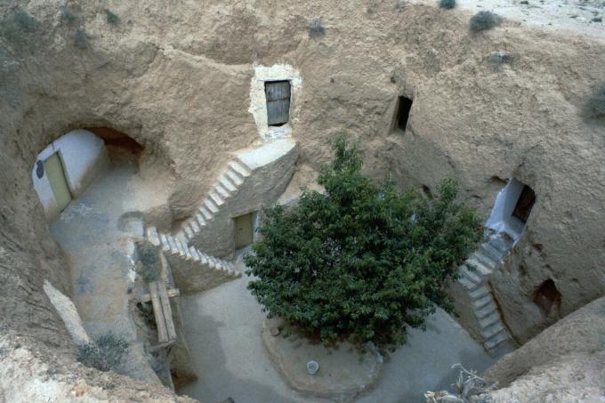 Treppen, Türen und Fenster bieten Zugang zu in die Erde gehauenen Wohnräumen - ein Baum steht im Zentrum der Tagebaugemeinschaft