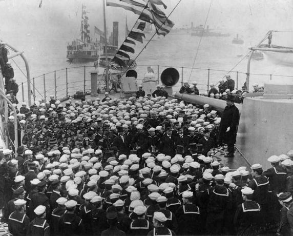 Präsident Theodore Roosevelt steht auf einem Schlachtschiff-Turm mit einer Menge Seeleute vor ihm.