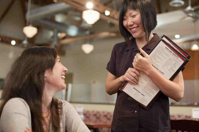 Eine Kellnerin mit Menüs in der Hand im Gespräch mit einem Kunden.