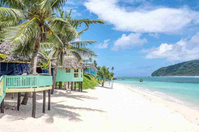 Blick entlang des Lalomanu Beach, Upolu Island, Samoa, auf farbenfrohe samoanische Strandhütten, die eine Alternative zu Hotel- oder Resortunterkünften darstellen