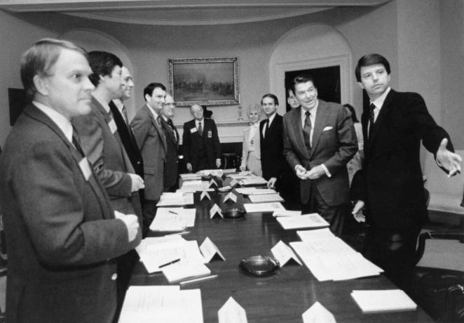 Ein Schwarz-Weiß-Bild von Ronald Reagan und mehreren anderen Männern in Anzügen an einem langen Konferenztisch