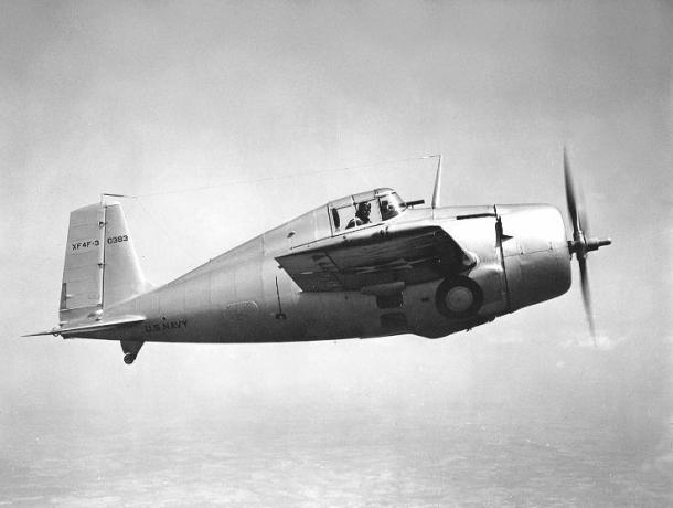 Grumman XF4F-3 Wildcat fliegt von links nach rechts, silbernes Aluminium-Finish, Pilot schaut hinaus.