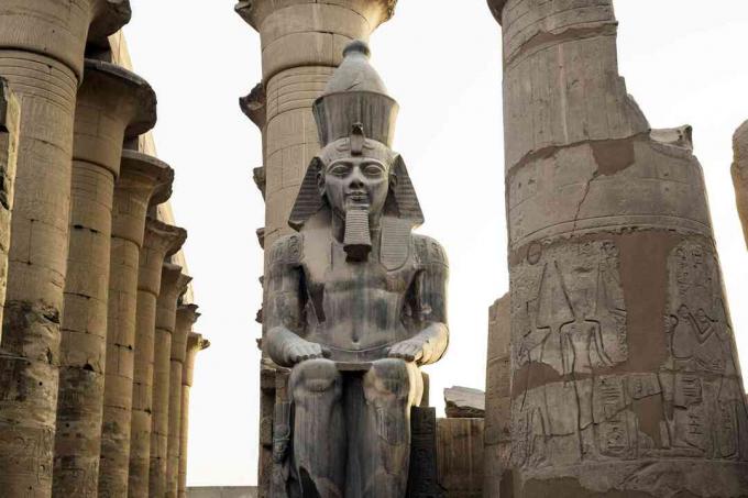 Statue von Ramses II, die zwischen Steinsäulen sitzt